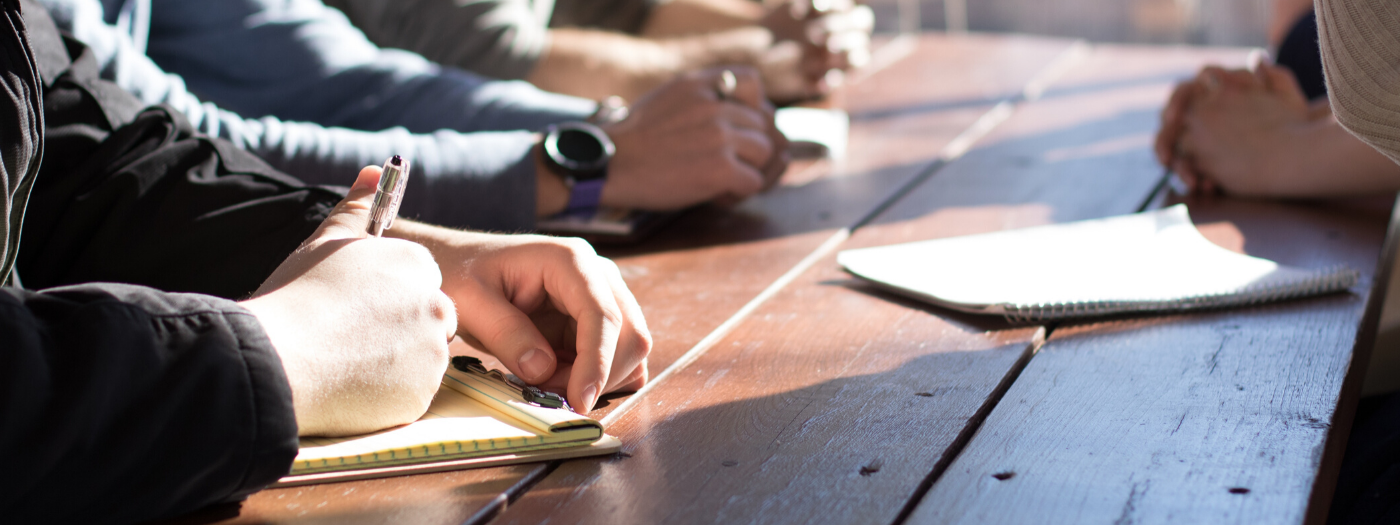 group of people working together at a desk, taking notes