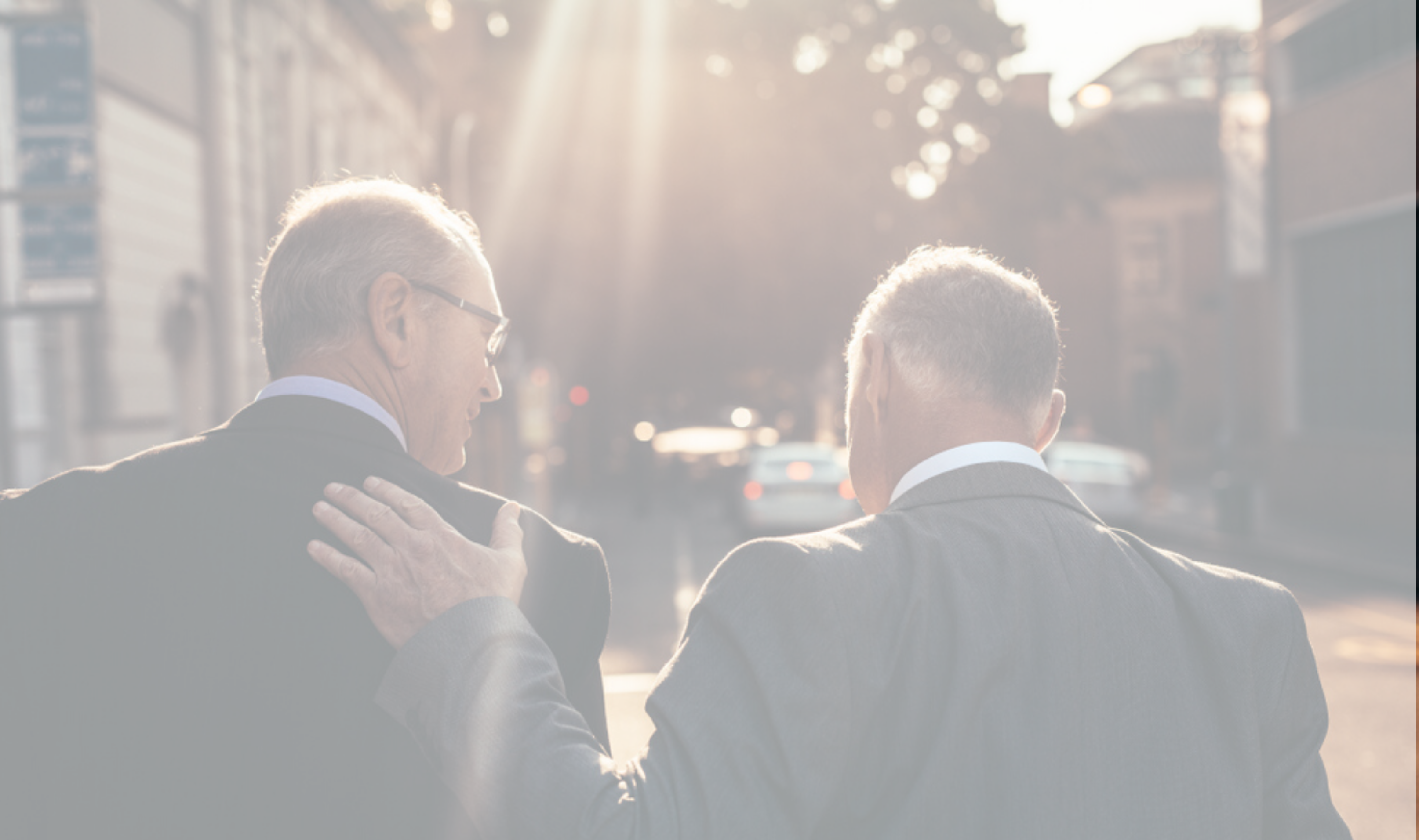 2 professional men walking down a sunny street, patting one another on the back