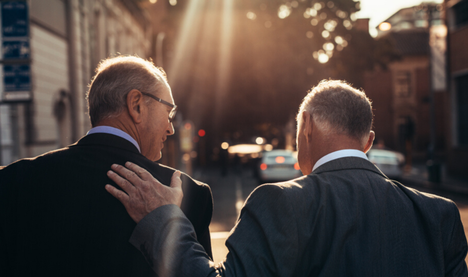 two professional business men walking down a sunny street and patting each other on the back