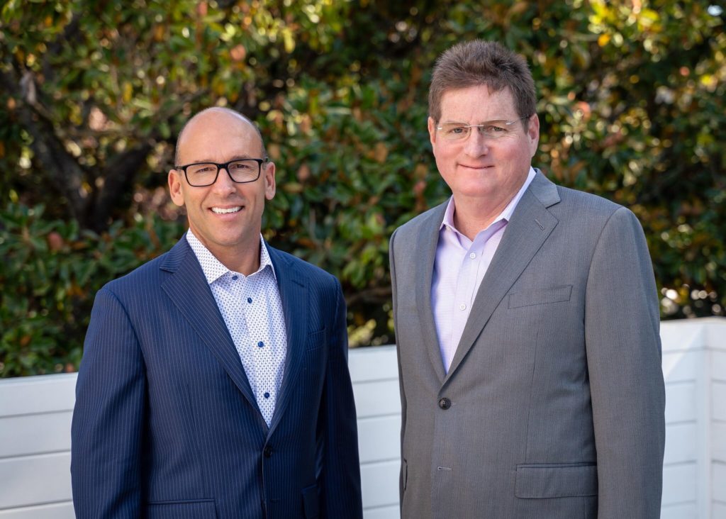 Allworth co-CEOs and co-founders Scott Hanson and PAt McClain wearing suits and smiling in a sunny garden