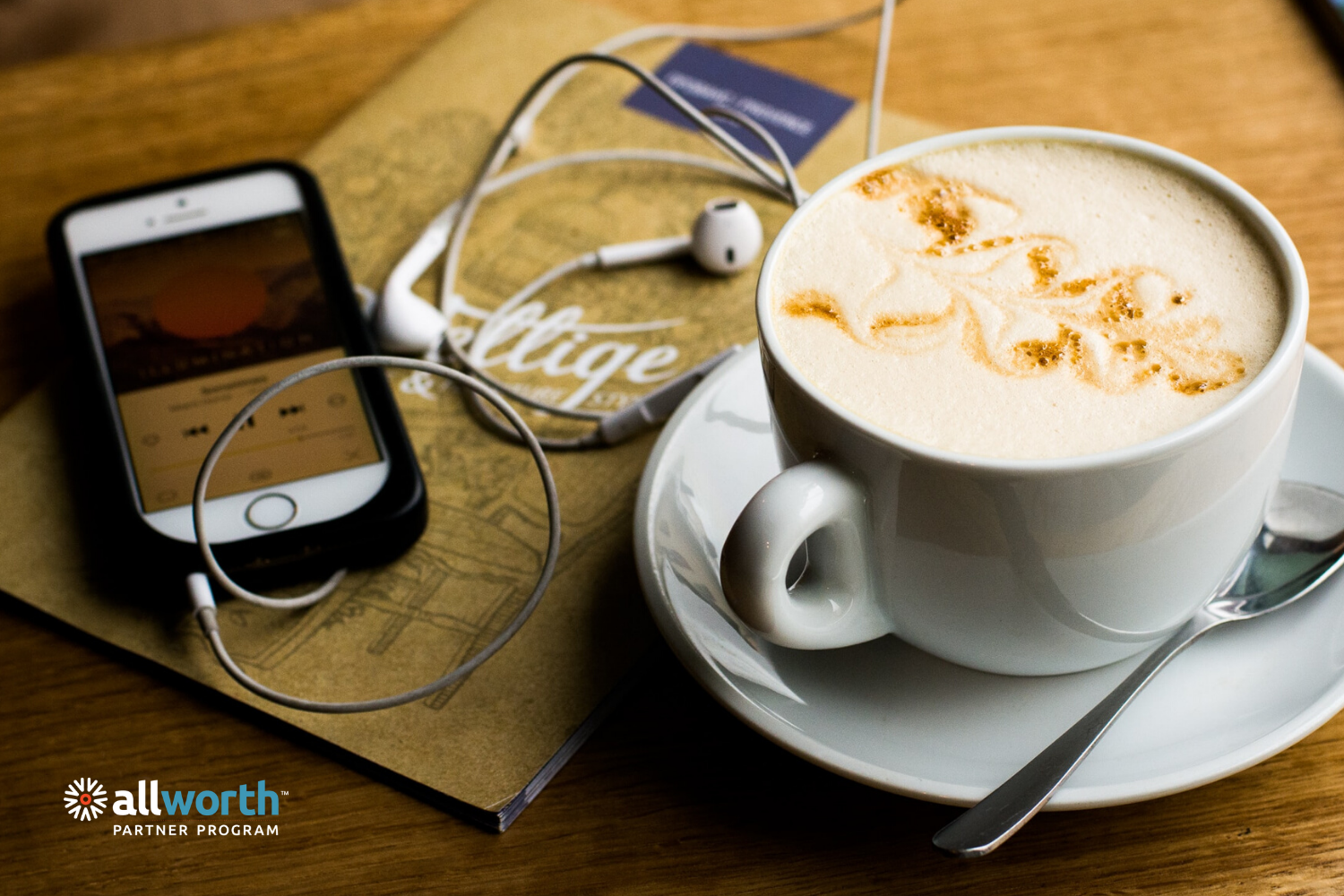cell phone with headphones plugged in, on a desk next to a warm cappuccino