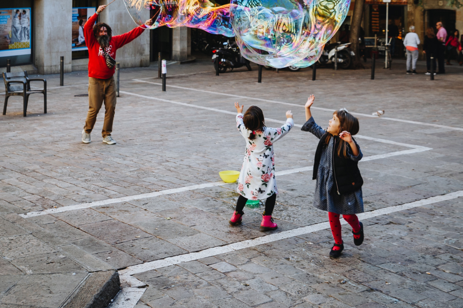 happy children running around a plaza, playing with large bubbles