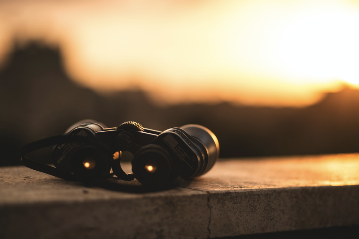 a pair of binoculars sitting on a wall, with a sunset background