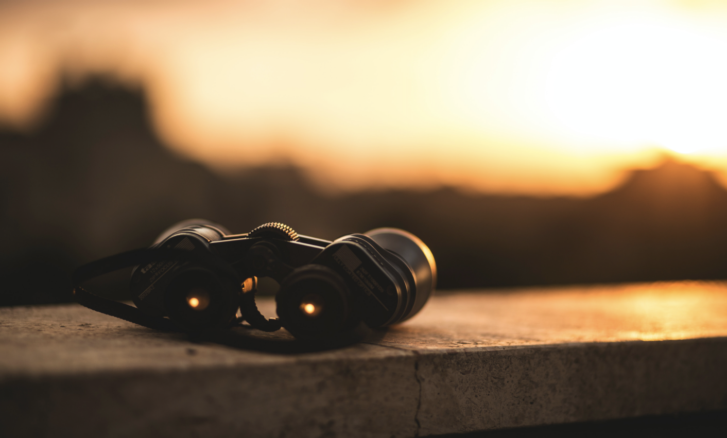 a pair of binoculars sitting on a wall, with a sunset background