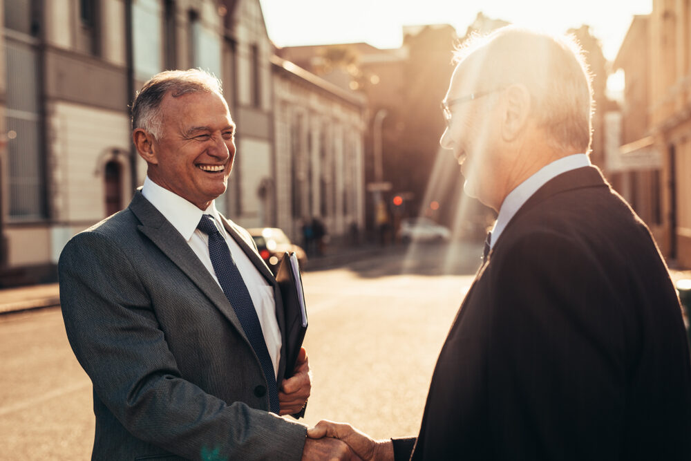 2 professional business men shaking hands on an open street