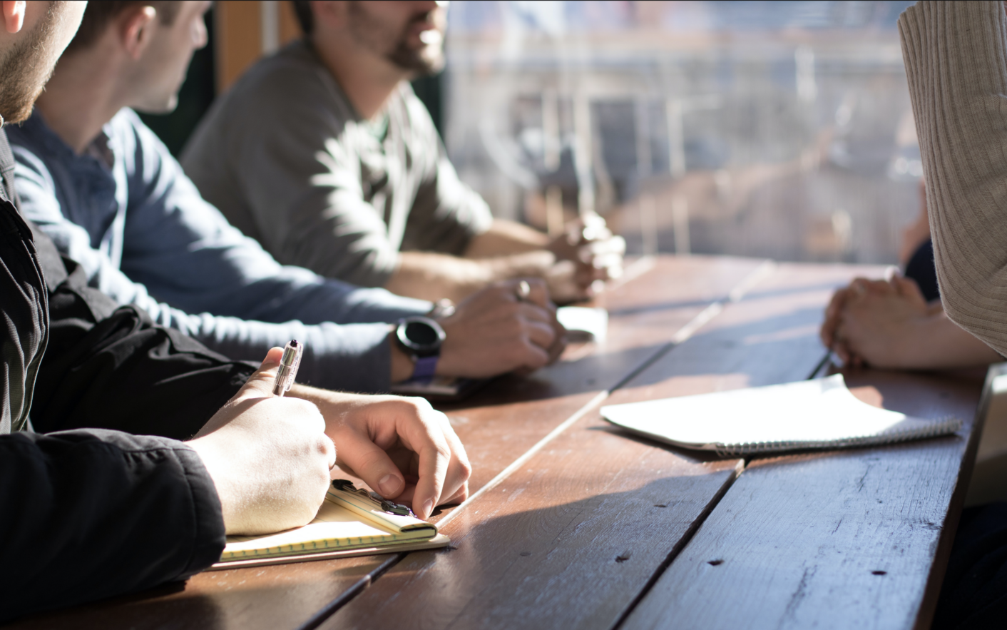 group of 4 people having a meeting at a desk next to sunny high-rise window