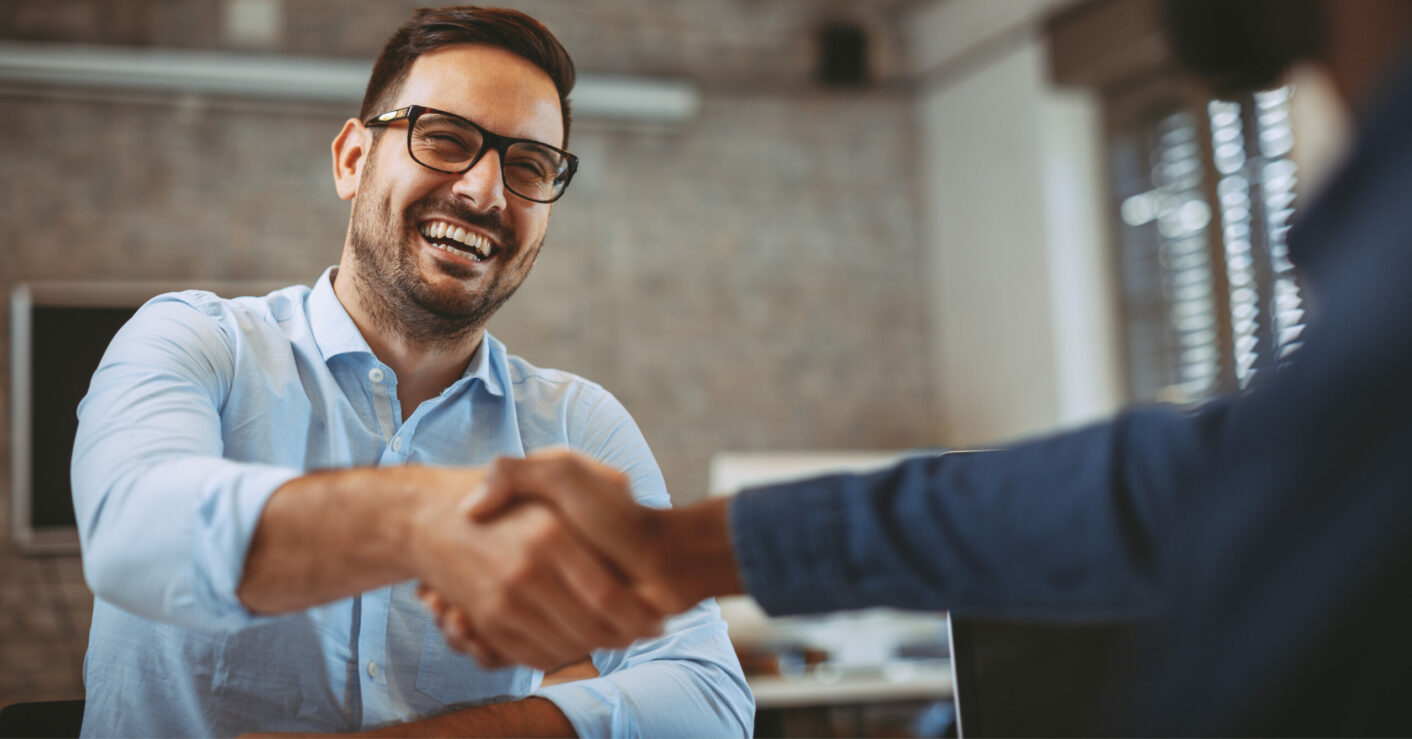 Man smiling and shaking a person's hand